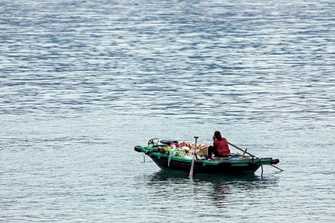A person sits in a small boat on a calm lake surrounded by blue water, woman in a rowing boat in