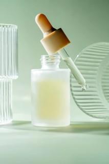 A serum dropper bottle stands against a serene pastel green background, with a droplet poised at