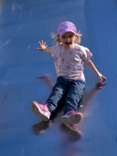 Little girl, 3 years, blonde, baseball cap, logo NYY New York Yankees, slides on slide, playground,