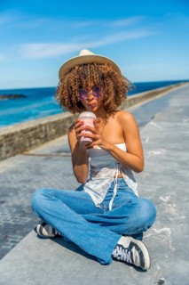 Vertical full length photo of a latin young woman with curly hair sipping a milkshake with a straw