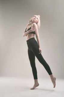 Young slim female model in black bra and leggings standing on tiptoe and covering breast with hands