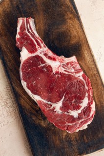 Raw rib eye steak, cowboy steak, wooden chopping board, marble table, top view, no people