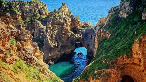Impressive cave and rock formations with a boat with tourists exploring the coastline, Ponta da