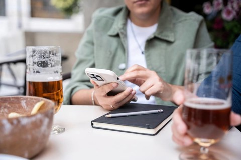 Lesbian couple at a bar chatting while drinking beers. A woman uses a smartphone next to a notebook