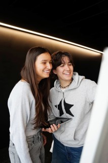 Two teenagers, one non-binary with short hair and one female with long hair, share a joyful moment