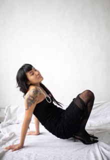 Elegant portrait of a young Asian woman in a black dress, sitting gracefully. Her expression is
