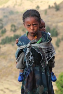 In the highlands between Mekele and Lalibela, girl carries sibling on her back, Ethiopia