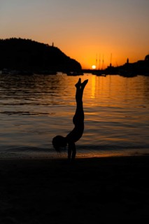 A stunning silhouette of a child performing a handstand on a beach during sunset in Soller, Majorca