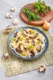 Rice noodles with champignons mushrooms, egg sauce and oregano on blue ceramic plate on a gray