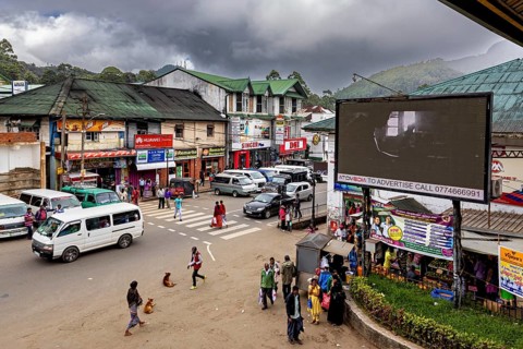 Lively road junction with traffic and billboards against a mountainous backdrop, Nuwara Eliya Sri