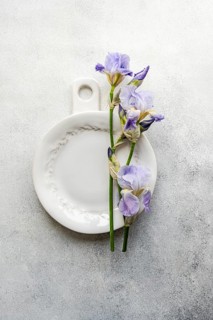 Top view of beautiful violet iris flowers arranged on an elegant white ceramic plate over a
