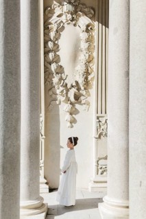 A young girl in a First Communion dress stands gracefully among grand architectural columns and