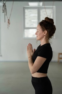 A serene woman stands in a yoga pose with palms together, eyes closed, focusing on mindfulness in a