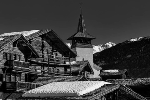 Snow-covered roofs of old farmhouses and barn storage, in the back the church tower of the Saint