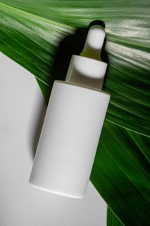 A white cosmetic dropper bottle rests on a vibrant green leaf, highlighting natural and sustainable