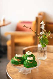 Three matcha choux pastries on a glass plate highlight this cozy cafe setting with a wooden table