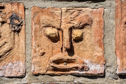 Artistic installation with mask and facial reliefs made of terracotta, in a historic brick wall,