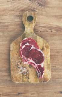 Raw rib eye steak, cowboy steak, on a wooden chopping board, top view, no people
