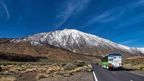 A coach travels along a road that passes a snow-covered mountain, Teide, Parque Nacional del Teide,