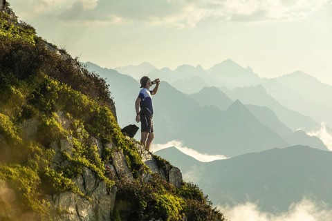 A man pauses on a scenic mountain trail, taking a moment to hydrate during his run. He stands amid