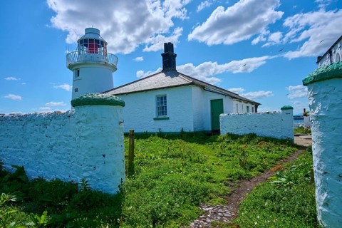 White lighthouse next to green garden and historic house under sunny sky, Inner Farne Lighthouse,