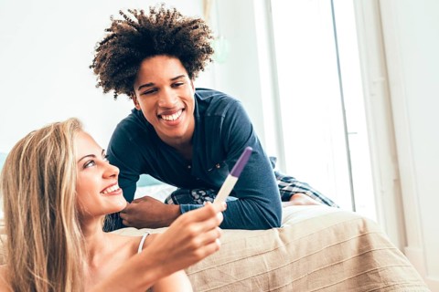 A happy couple smiling at a positive pregnancy test in a sunlit room. The image captures the