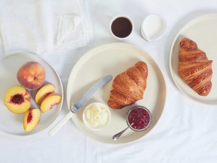 Continental breakfast served on white tablecloth: croissants, butter, jam, cup of coffee and fresh