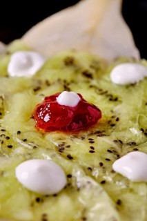 A close-up of a fresh kiwi and pear dessert with small dollops of yogurt and a dollop of red berry