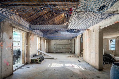 An indoor construction site with exposed concrete walls, safety netting, scaffolding, and