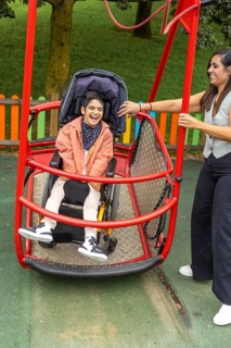A child with cerebral palsy in a wheelchair enjoys an inclusive playground swing, assisted by a
