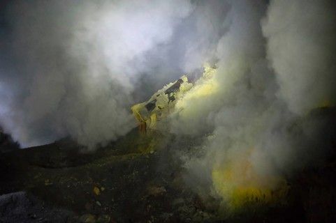 Thick sulfur smoke rises from Ijen's crater vents, with visible yellow mineral deposits formed by
