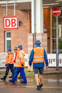 Construction workers in protective waistcoats and helmets in front of a DB building on the road,