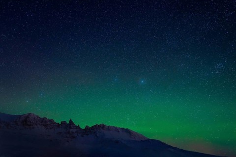 The stunning Northern Lights illuminate the starry sky above a snowy mountain range in Iceland,