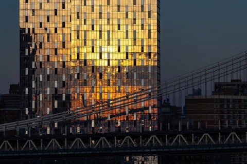 Golden sunlight reflects off a modern skyscraper in New York, creating a brilliant pattern