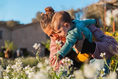 A mother and her child enjoy a sunny day in a garden, exploring white flowers. The moment captures