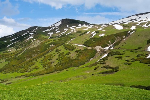 Green hills with snow-covered areas under blue sky and some clouds, Zagari Pass, Svaneti, Greater