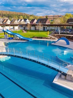 Complex outdoor pool with bridge and slide, surrounded by a picturesque landscape, Calw Stammheim