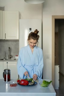 A woman in a light blue robe prepares a healthy breakfast in her kitchen, surrounded by fresh