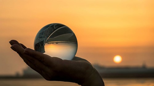 A hand holds a crystal ball, capturing the sunset vibrant colors and ocean horizon in Porto,