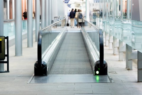 A contemporary urban scene featuring a moving walkway in a busy public transportation station with