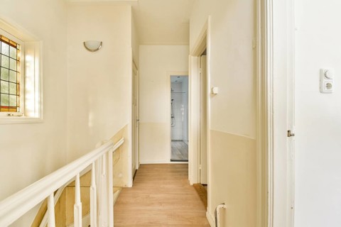 A spacious hallway featuring white walls, natural light, and wooden flooring, designed for a clean