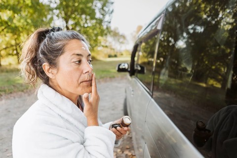 A woman engages in her skincare routine beside her van amid New Zealand autumn scenery. Surrounded