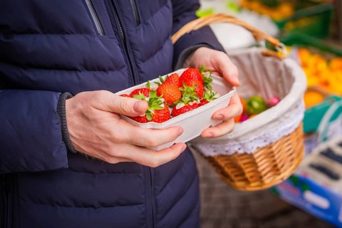 Hands holding bowl of fresh strawberries, next to a basket with other purchases, Easter campaign,