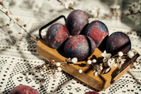 Artistic Easter eggs with a cosmic paint theme are displayed on a wooden tray surrounded by cherry