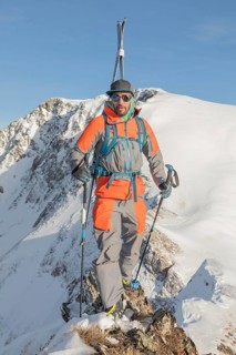 Ski tourer in bright gear standing on snowy ridge, basking in winter sunlight. The mountain view