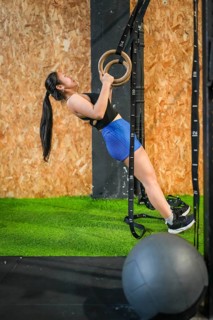 Vertical full length profile of an asian strong woman working out using gym rings alone in a modern