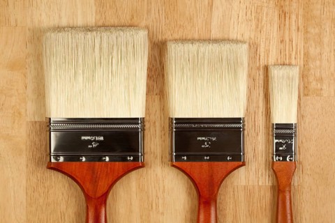 Three Different Sized New Paint Brushes on a Wood Surface