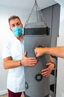 Physiotherapist with mask holding punching bag. Physiotherapy with protective measures for the