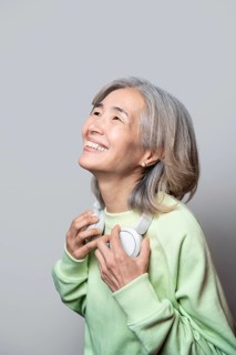 Asian senior woman wearing a light green sweater and headphones, looking up with a joyful