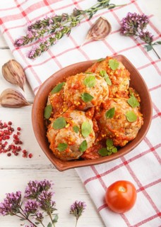 Pork meatballs with tomato sauce, oregano leaves, spices and herbs in clay bowl on a white wooden